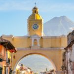Arco de Santa Catalina sobre la 5.ª avenida Norte de Antigua Guatemala, con su torre del reloj amarilla y el volcán de Agua al fondo