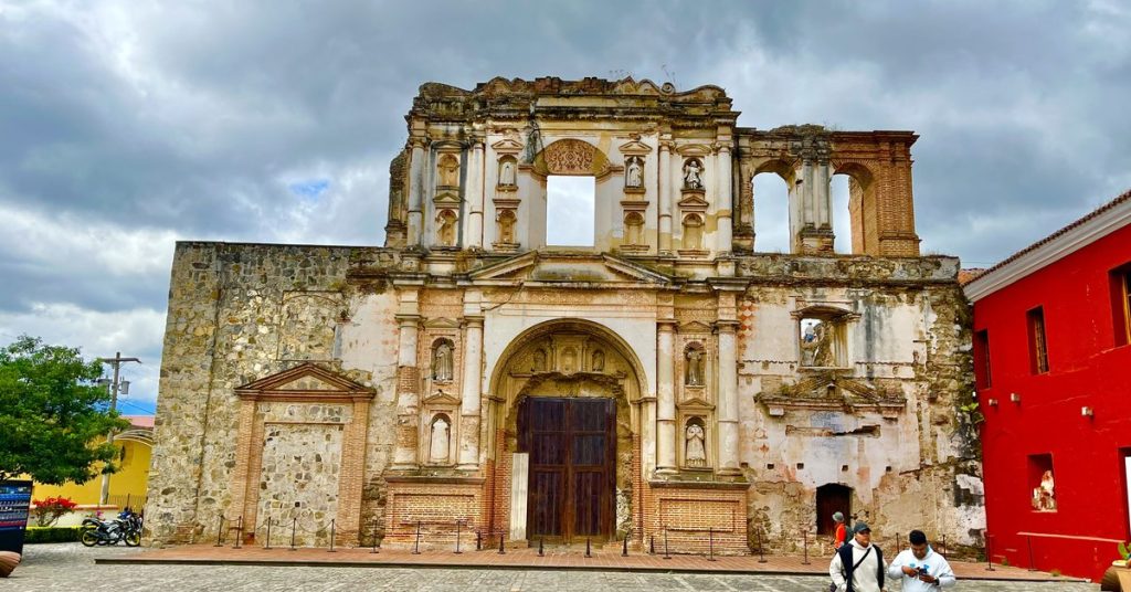 Fachada en ruinas de la iglesia de la Compañía de Jesús en Antigua Guatemala, con nichos de santos, portón de madera y ventanas abiertas al cielo, sede del Centro de Formación de la Cooperación Española