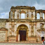 Fachada en ruinas de la iglesia de la Compañía de Jesús en Antigua Guatemala, con nichos de santos, portón de madera y ventanas abiertas al cielo, sede del Centro de Formación de la Cooperación Española